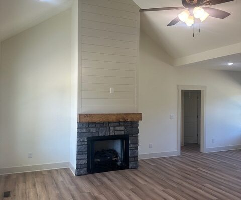 Living room fireplace with stone surround, wood mantel, and shiplap accent wall