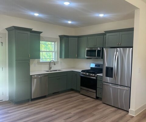 Kitchen with green cabinets, quartz countertops, and stainless steel appliances