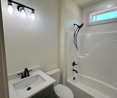 Guest bathroom with green vanity, quartz countertop, and tub-shower combination